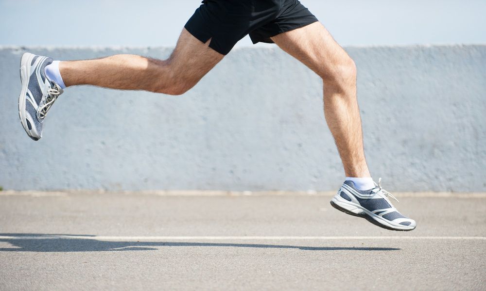 Mid-stride action shot of a runner wearing grey and blue athletic sneakers.